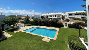 Una piscina rodeada de un césped cuidado, con vistas a edificios blancos al fondo.