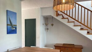 Un comedor con una mesa y sillas de madera, una puerta verde, una escalera y luces fijadas en la pared.