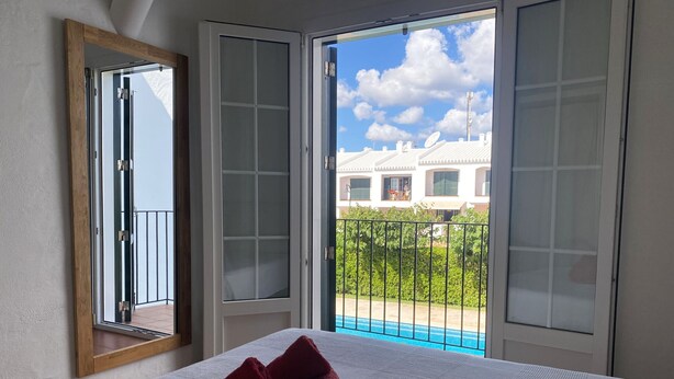 Una habitación de hotel con una cama, un ventanal con vistas a una piscina y edificios, y un espejo en la pared.
