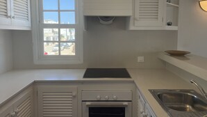 A compact kitchen with white cabinetry, a built-in oven, a sink, and a window providing a view of the street. - Apartment in Fornells (Fornells)