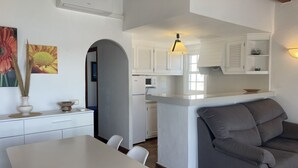 A modern kitchen with white cabinets, a central island, and a dining area with a white table and chairs. - Apartment in Fornells (Fornells)