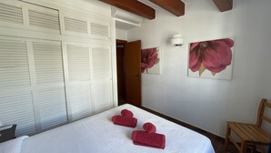 A hotel room with a bed, a wooden chair, a white door with louvered panels, and two wall-mounted lamps. - Apartment in Fornells (Fornells)