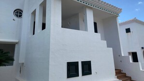 A white building with a balcony, multiple windows, and a staircase leading to an upper floor.