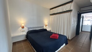 Ein Hotelzimmer mit einem Bett, zwei Wandlampen, einem Vorhangfenster und einem Fliesenboden.