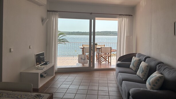 Ein Wohnzimmer mit einer Couch, einem Fernseher und einem Balkon mit Tisch und Stühlen.
