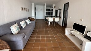 Ein Wohnzimmer mit grauem Sofa, Fernseher und einem Essbereich mit Tisch und Stühlen.