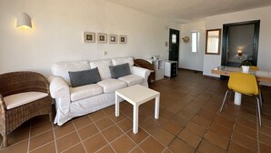 A living room with a white sofa, a small white table, a wicker chair, a yellow chair, and a dining table. - Beautiful apartment in very front of the sea (Fornells)