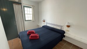 A bedroom with a bed, two wall-mounted lamps, a window with curtains, and a green door. - Beautiful apartment in very front of the sea (Fornells)