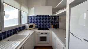 Een compacte keuken met witte kasten, een magnetron, een fornuis en een koelkast.