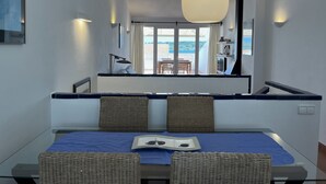 Een moderne kamer met een eettafel, rieten stoelen, een groot raam met uitzicht en een hanglamp.