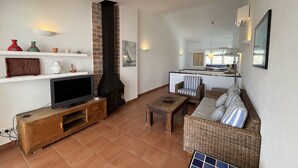 Een woonkamer met een tv, open haard, bank en een keuken op de achtergrond.