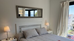 A hotel room with a bed, two bedside lamps, a bedside table, a mirror, and a view of the outside. - Superb luxury house in front of the sea (Fornells)