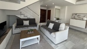 A modern living room with a staircase, two sofas, a coffee table, and a television. - Superb luxury house in front of the sea (Fornells)
