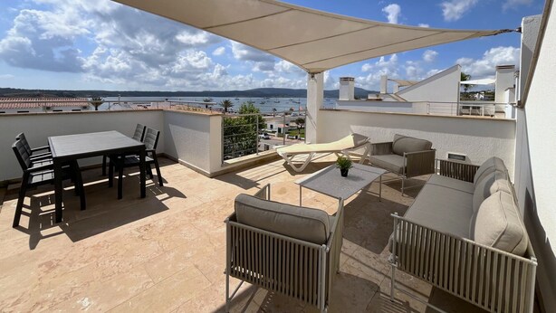 A rooftop terrace with a table and chairs, a small table with a plant, and a view of the sea and boats. - Superb luxury house in front of the sea (Fornells)