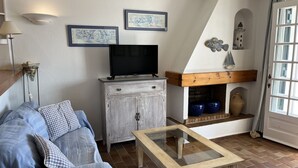 En hyggelig stue med en sofa, et sofabord med glasplade, et fjernsyn på et træskab og en pejs med dekorative genstande.