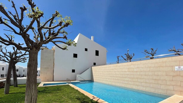 Una piscina con agua azul cristalina, rodeada de césped y un edificio blanco con múltiples ventanas.