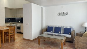 Un espacio habitable compacto con zona de comedor, kitchenette y sofá con cojines.