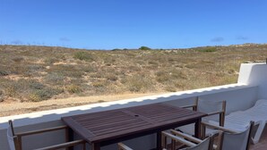 Una terraza con mesa y sillas de madera, con vistas a un paisaje seco y vegetación escasa.