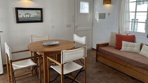 Ein gemütliches Zimmer mit einem Holztisch, weißen Stühlen, einer Couch mit Kissen und einem Fenster mit Vorhängen.