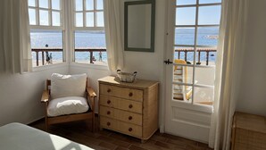 Ein Schlafzimmer mit Bett, Kommode und zwei Fenstern mit Meerblick.