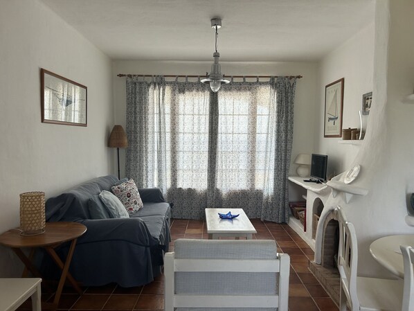 A living room with a sofa, a small table, a chair, a fireplace, and a window with curtains.