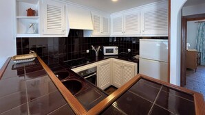 Una cocina con armarios blancos, baldosas negras, un microondas, una estufa y un refrigerador.