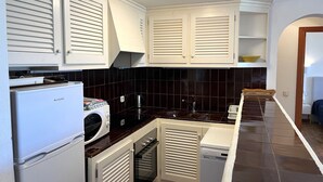 Una cocina compacta con armarios blancos, lavadora, lavavajillas y microondas.