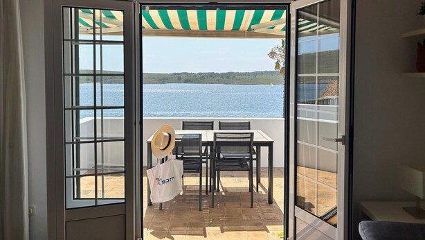 An open door leading to a balcony with a table, chairs, a hat, and a bag. - Apartment with sea views and pool in Fornells (Fornells)