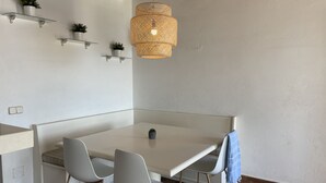 A modern dining area with a white table, two grey chairs, a hanging woven light fixture, and small potted plants on wall-mounted shelves. - Apartment with sea views and pool in Fornells (Fornells)