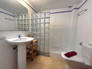Et badeværelse med en hvid vask, en brusekabine i glas, toilet og et spejl.