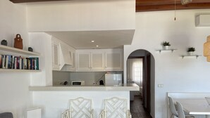 A modern kitchen with white cabinets, a dining area with a white table and chairs, and a small bookshelf with books. - Apartment with sea views and pool in Fornells (Fornells)