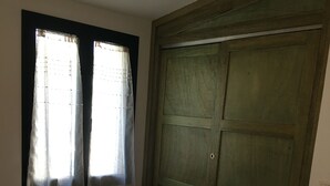 Une chambre avec un lit, deux fenêtres avec des rideaux et une armoire en bois.