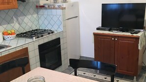 Une cuisine de taille réduite, équipée d’une cuisinière à gaz, d’un réfrigérateur et d’un téléviseur posé sur un meuble en bois.