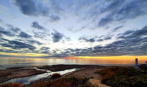 A beach with a path leading to the water, a rocky area, and a cloudy sky.
