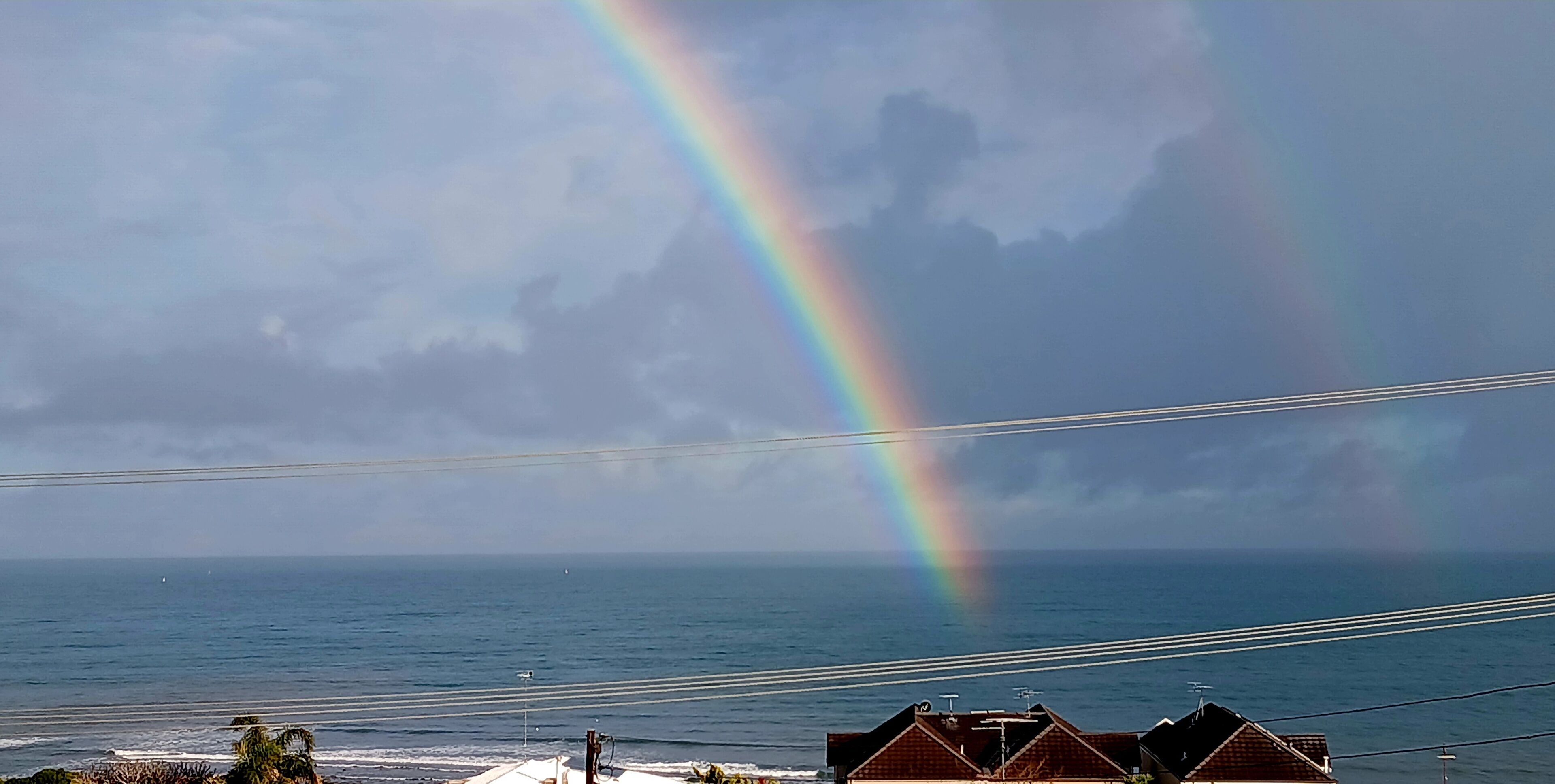 A coastal view with a rainbow, houses, and a clear sky.