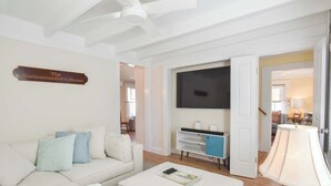 A living room with a white sofa, a coffee table, a TV, and a sign reading "The Stationmaster's House". - 5 Min Walk to Town, Patio, Yard, AC! (Provincetown)