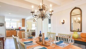 A dining area with a wooden table set for six, surrounded by chairs. A chandelier hangs above, and a mirror is on the wall. - 5 Min Walk to Town, Patio, Yard, AC! (Provincetown)