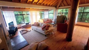 A spacious living room with a white sofa, a red armchair, and a television on a wooden stand. Large windows provide a view of the outdoors. - Quinta do Arquinho, River, Pool and Nature (Ponte de Lima)