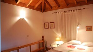 A bedroom with a wooden ceiling, a bed with floral bedding, a nightstand with a lamp, and two framed pictures on the wall. - Quinta do Arquinho, River, Pool and Nature (Ponte de Lima)