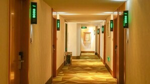 A hotel hallway with patterned carpet, wooden doors, and green directional signs. - Vatica Hefei Lujiang Road Hotel (Hefei)