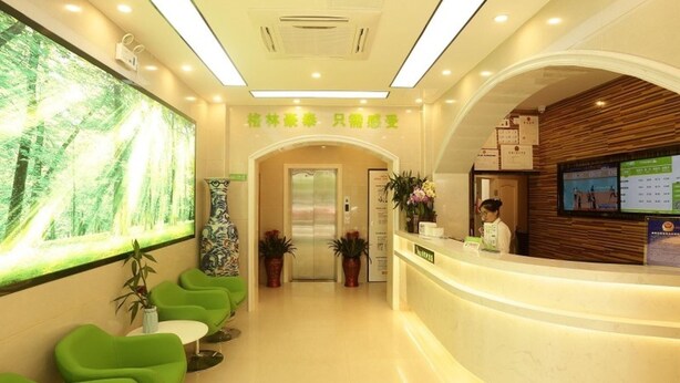 A modern reception area with a green seating area, a reception desk, and a large digital screen displaying information. - Vatica Hefei Lujiang Road Hotel (Hefei)