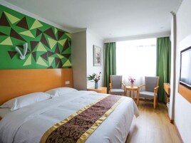 A hotel room with a large bed, a small table with chairs, a green curtain, and a geometric wall design.