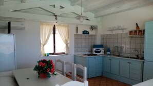 Une cuisine avec des meubles blancs, une fenêtre avec des rideaux, un ventilateur de plafond et une table avec des chaises.