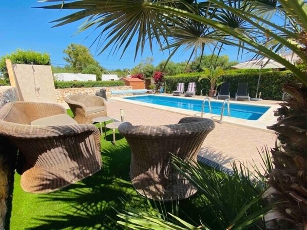 A pool area with wicker furniture and a stone wall.