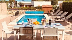 A poolside dining area with a table set for two, a pool, and lounge chairs.