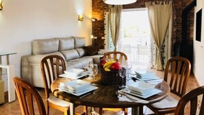 A dining area with a wooden table set for four, surrounded by wooden chairs. A grey sofa is positioned against the wall, and a large pendant light hangs above the table.