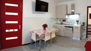 A compact kitchen with a red door, a dining table with chairs, a TV mounted above the counter, and a small island with a sink. - splendid two-room apartment with pergola (Bibione)