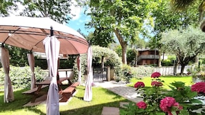 A gazebo with a picnic table, surrounded by a well-maintained garden with pink flowers and a stone pathway. - splendid two-room apartment with pergola (Bibione)