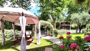 Un kiosque agrémenté d’une table de pique-nique, entouré d’un jardin bien entretenu où poussent des fleurs roses et qui est traversé par un sentier en pierre.