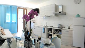 Una cocina compacta con armarios blancos, un lavamanos de acero inoxidable y un refrigerador pequeño.